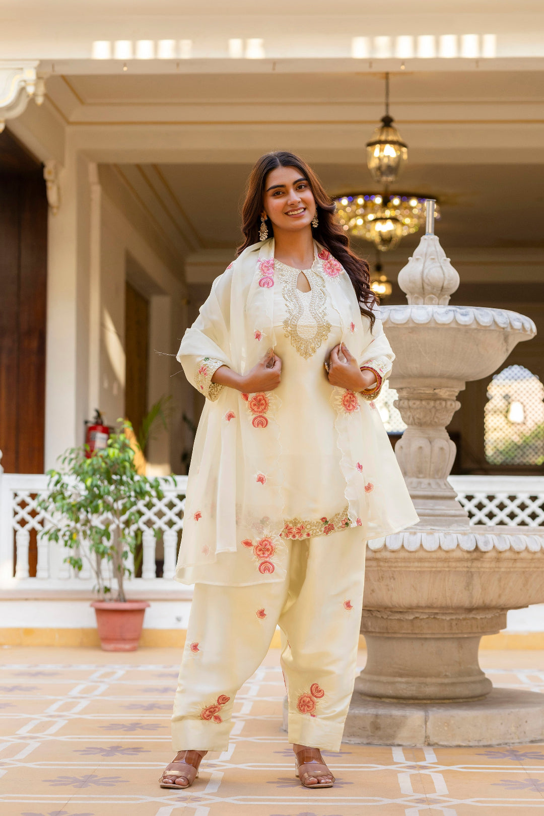 Woman in a traditional outfit standing in an elegant indoor setting with decorative elements.
