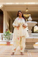 Woman in a traditional outfit standing in an elegant indoor setting with decorative elements.